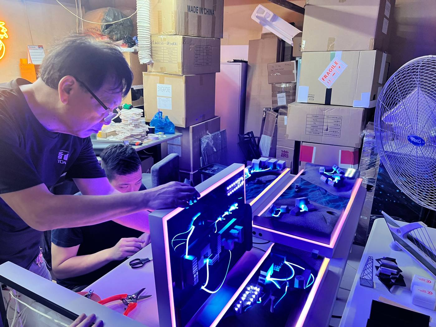Two Legion fabricators wiring an illuminated LED model build at night in the workshop