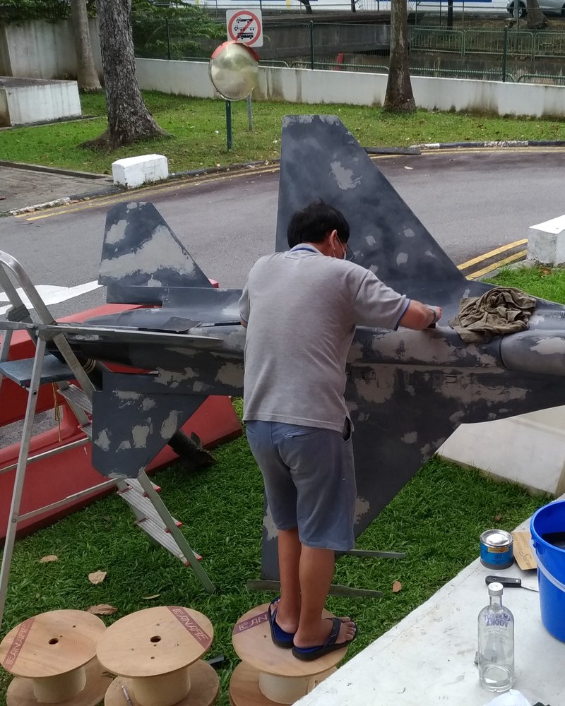 A full-size static display jet being stripped and resurfaced outdoors