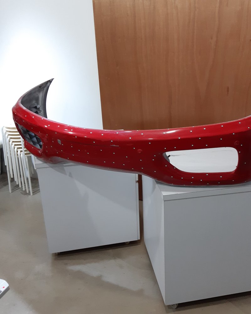 A red sports-car bumper covered in photogrammetry reference markers, resting in the workshop