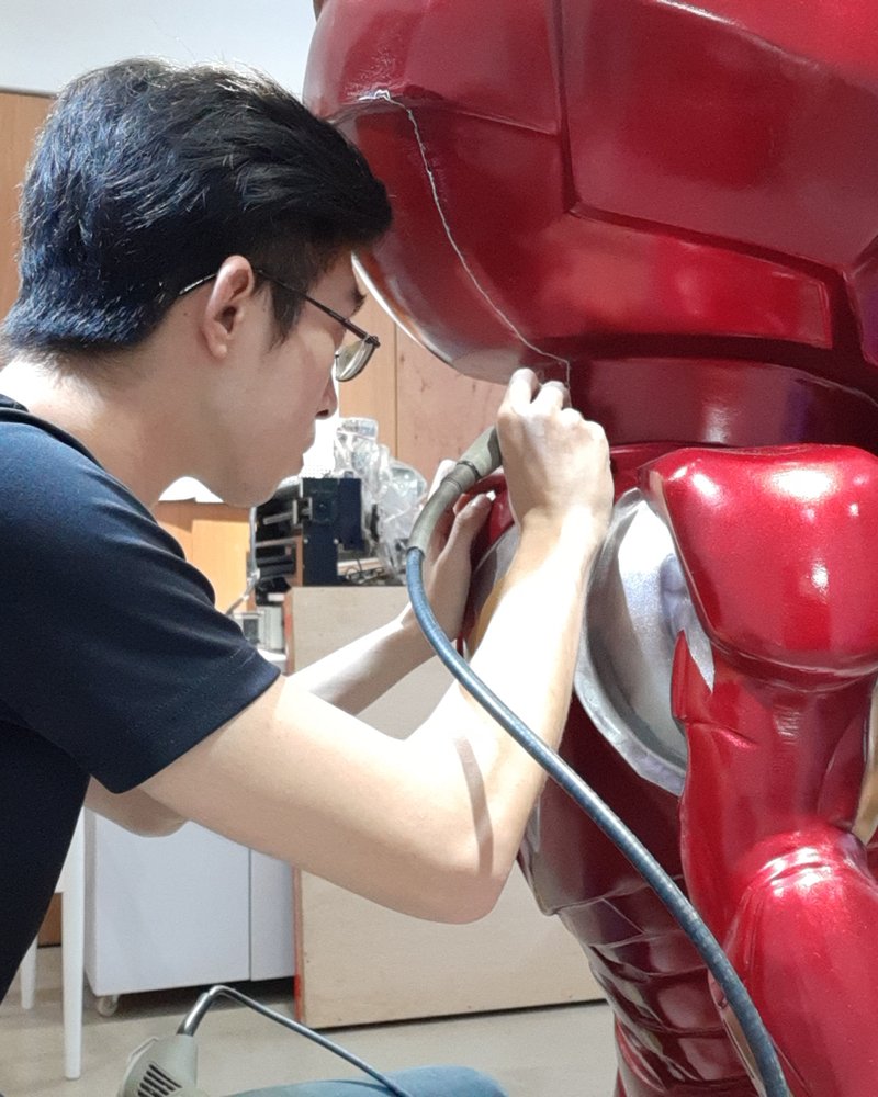 A maker reworking the cracked seam of a large fibreglass character statue with a rotary tool