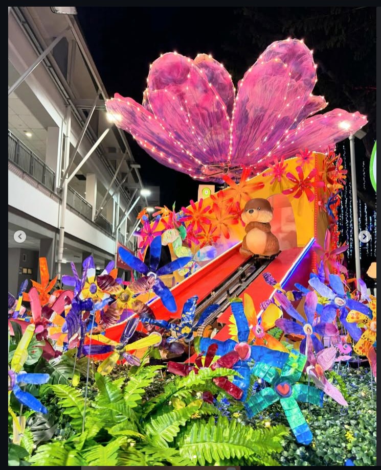 Illuminated Chingay parade float with a giant glowing flower and colourful pinwheels at night
